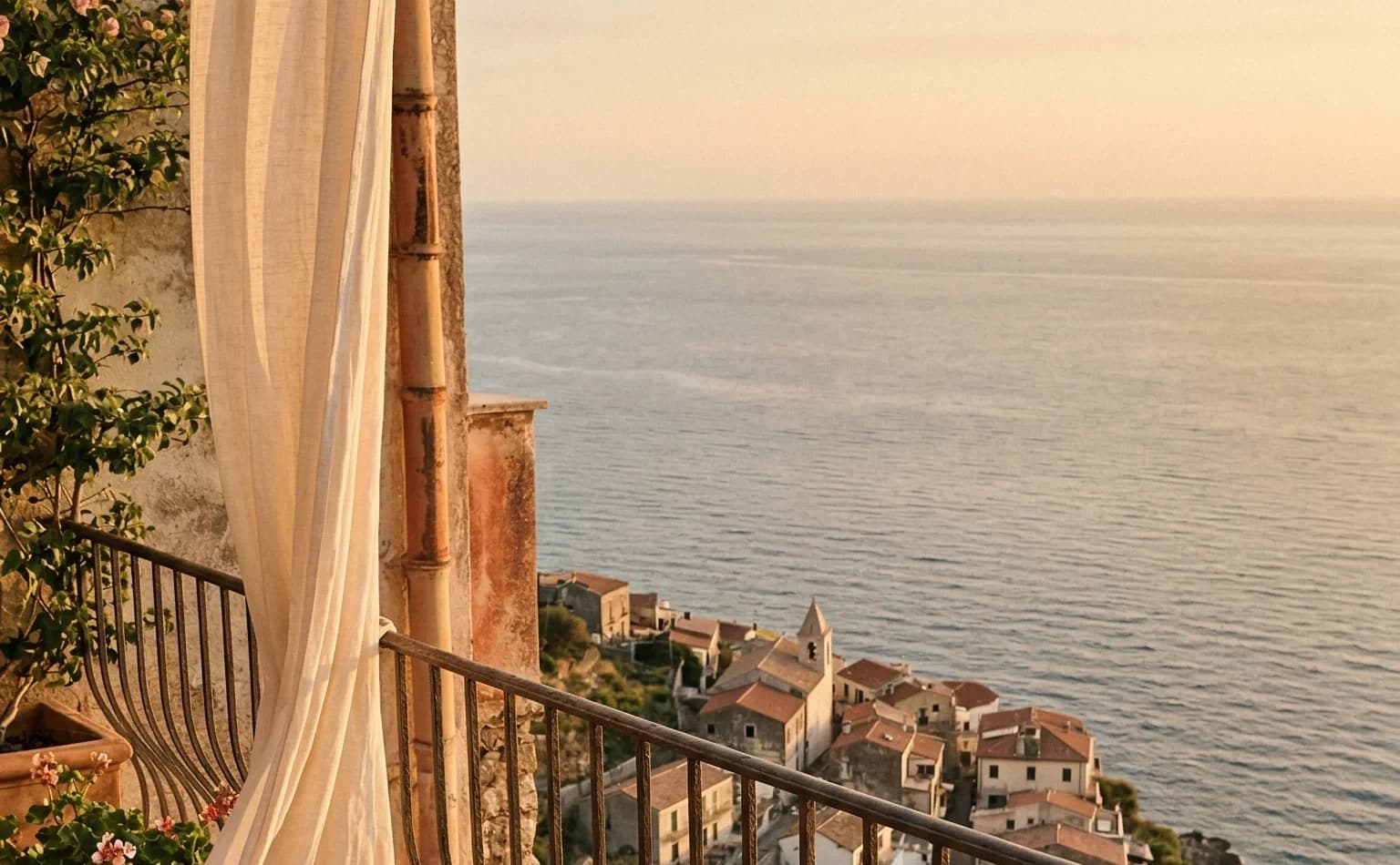 Villa terrace with linen curtain overlooking a coastal village at golden hour